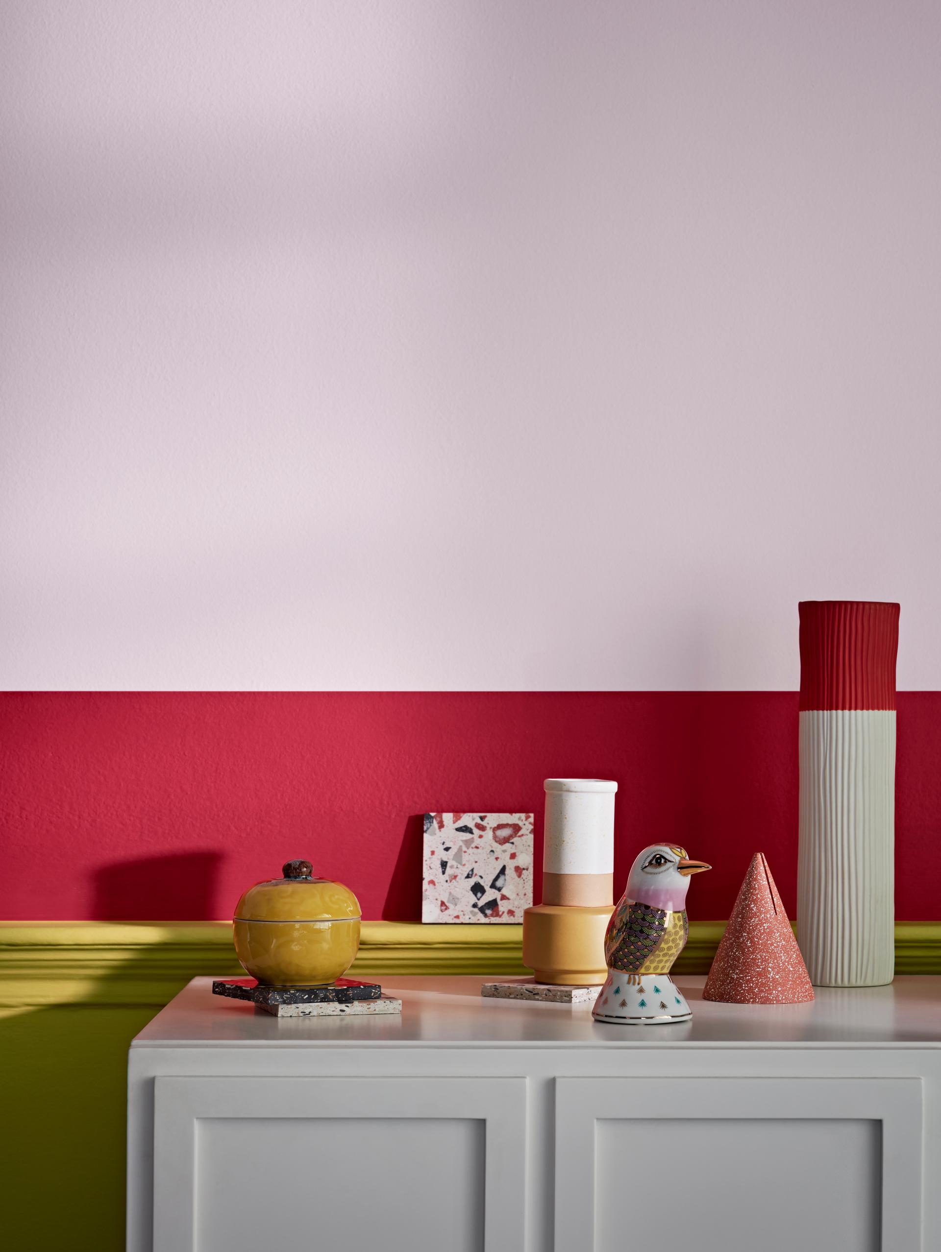 Colorful decorative items positioned on a white cabinet below a pink and red wall, showcasing workplace color importance.
