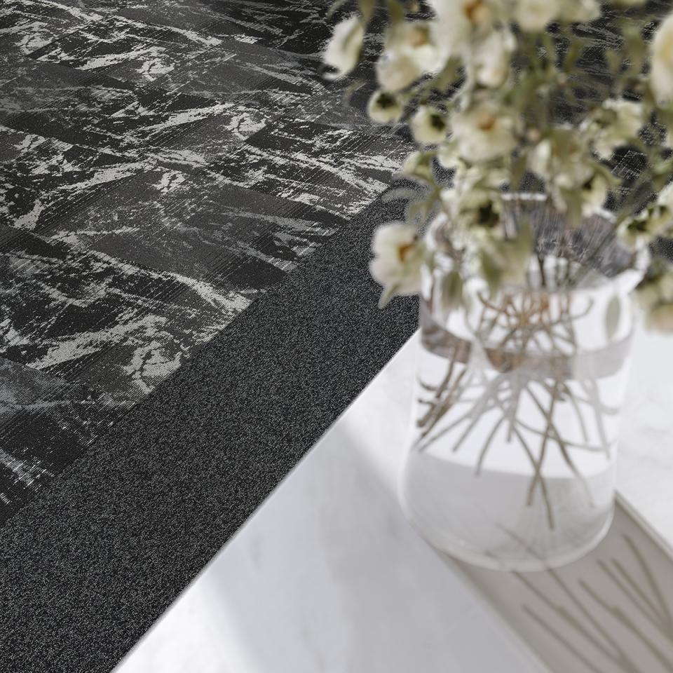 Sleek black and metallic carpet tiles from modulyss's Delight collection, displayed beside a vase of fresh flowers.