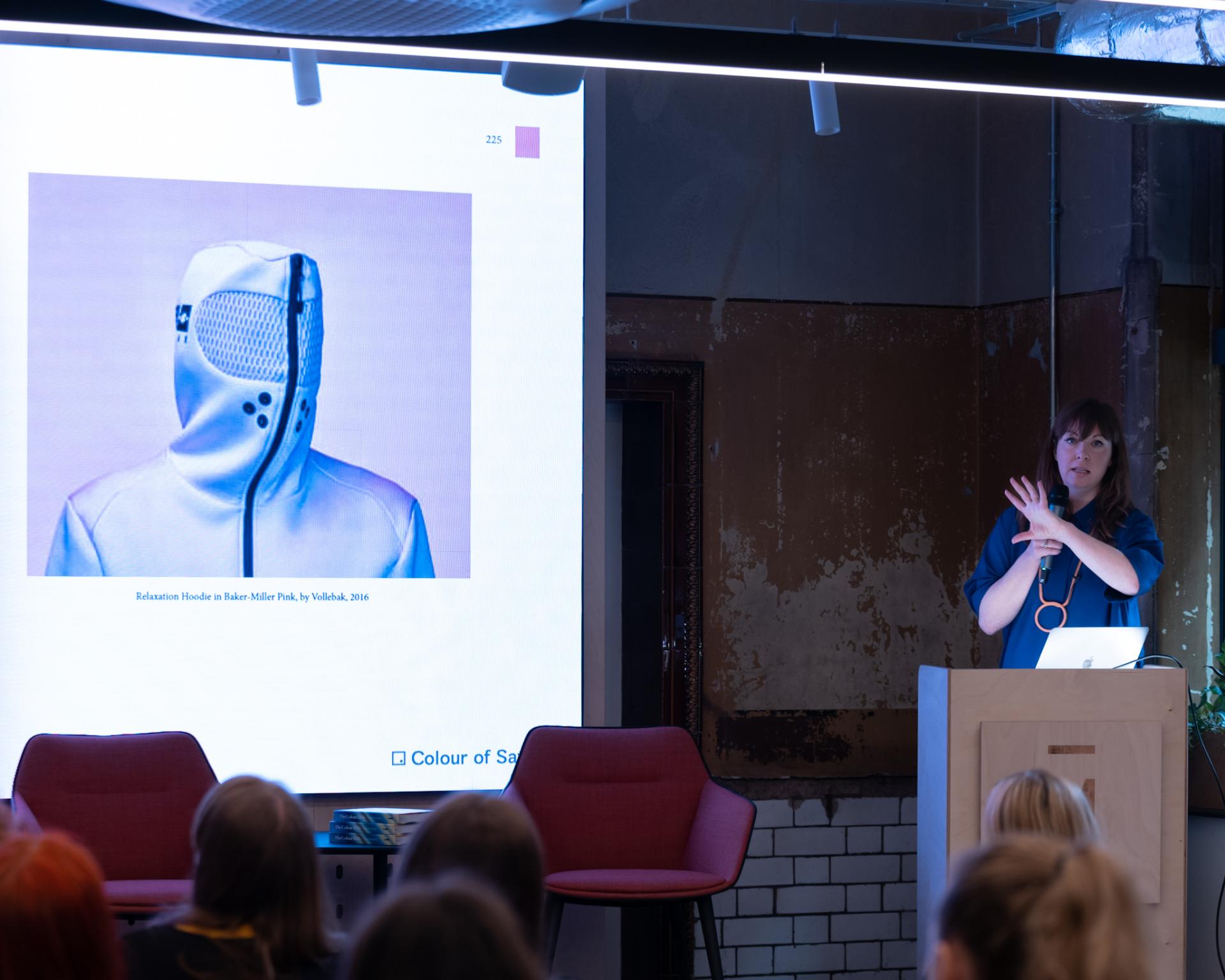 Laura Perryman presenting on colour theory and design concepts, with an image of a unique hoodie displayed behind her.