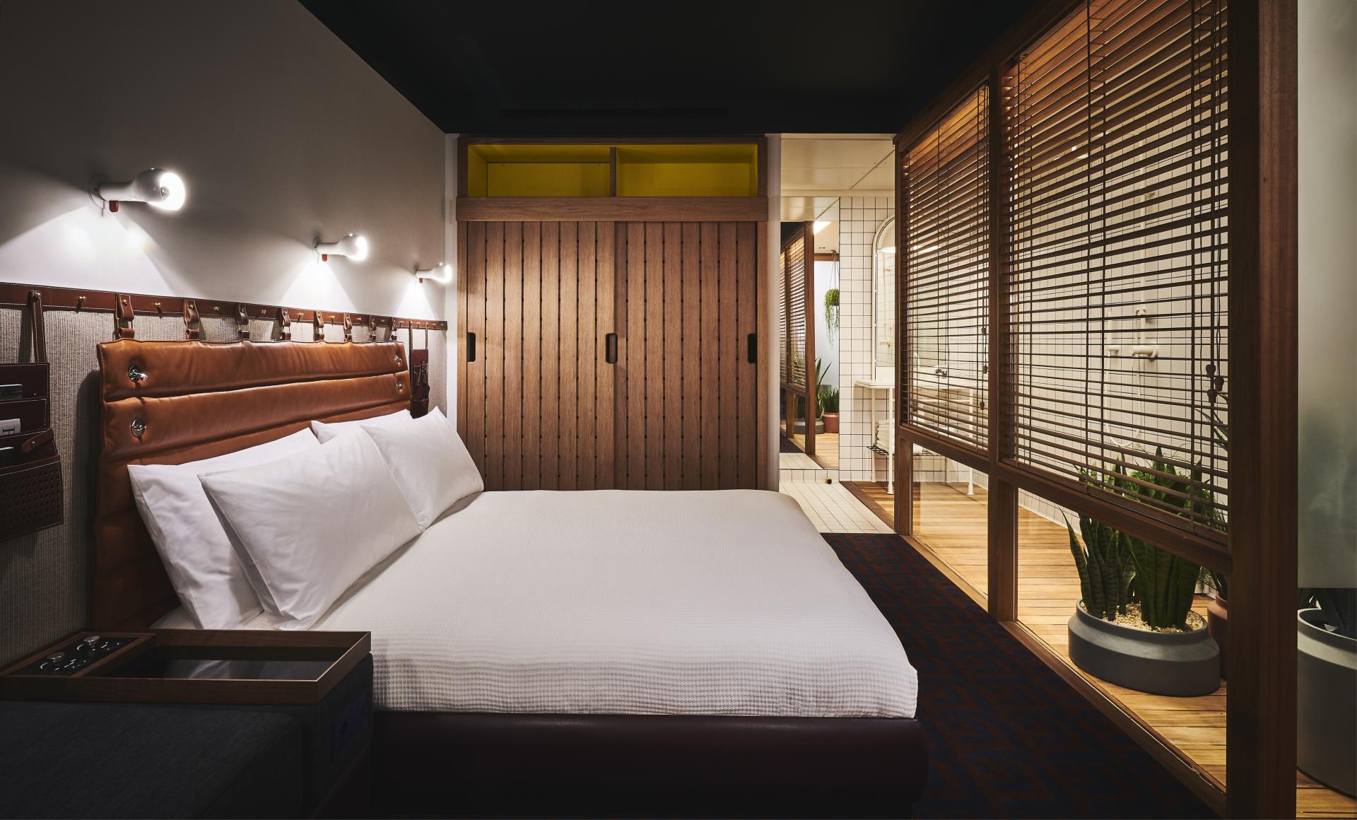 Modern hotel room at The Standard, London, featuring a stylish bed and partitioned bathroom area with natural elements.