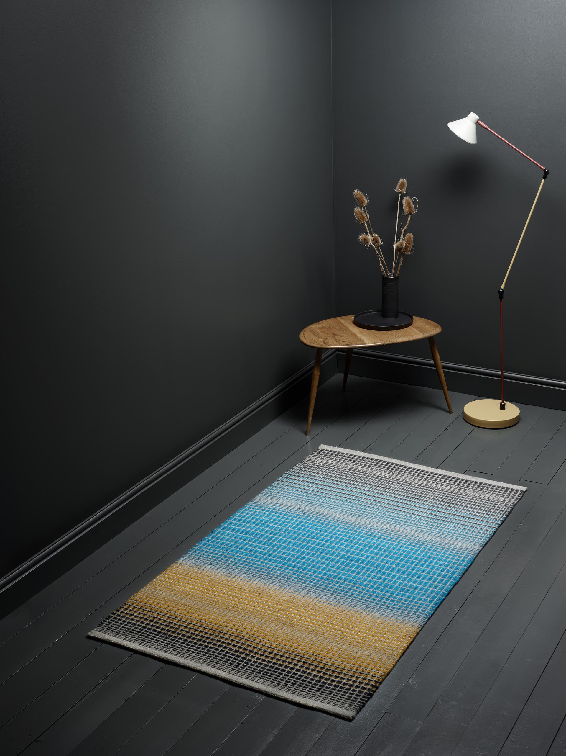 Scandinavian-inspired interior featuring a colorful geometric rug, stylish lamp, and modern wooden table with decorative plant.