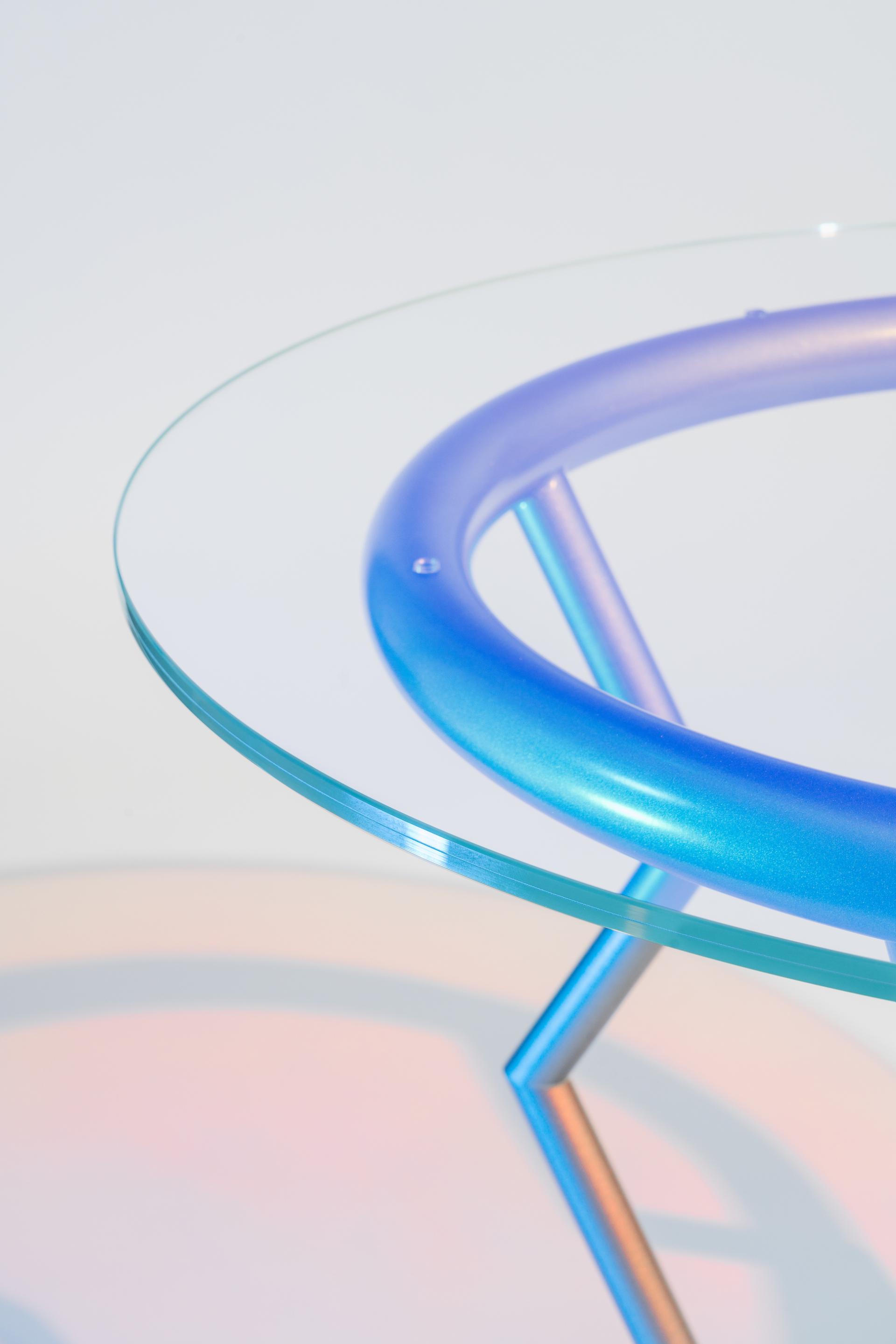 Table with a circular, blue gradient base and a clear glass top, showcasing Memphis design style.