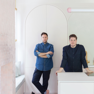 Interior designers Jordan Cluroe and Russell Whitehead pose in their modern kitchen, showcasing stylish materials and design elements.