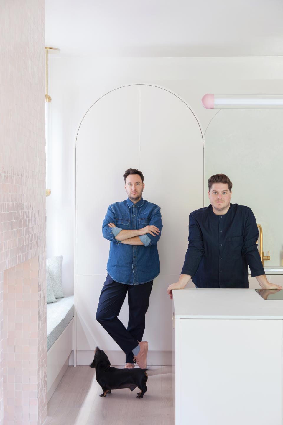 Interior designers Jordan Cluroe and Russell Whitehead pose in their modern kitchen, showcasing stylish materials and design elements.