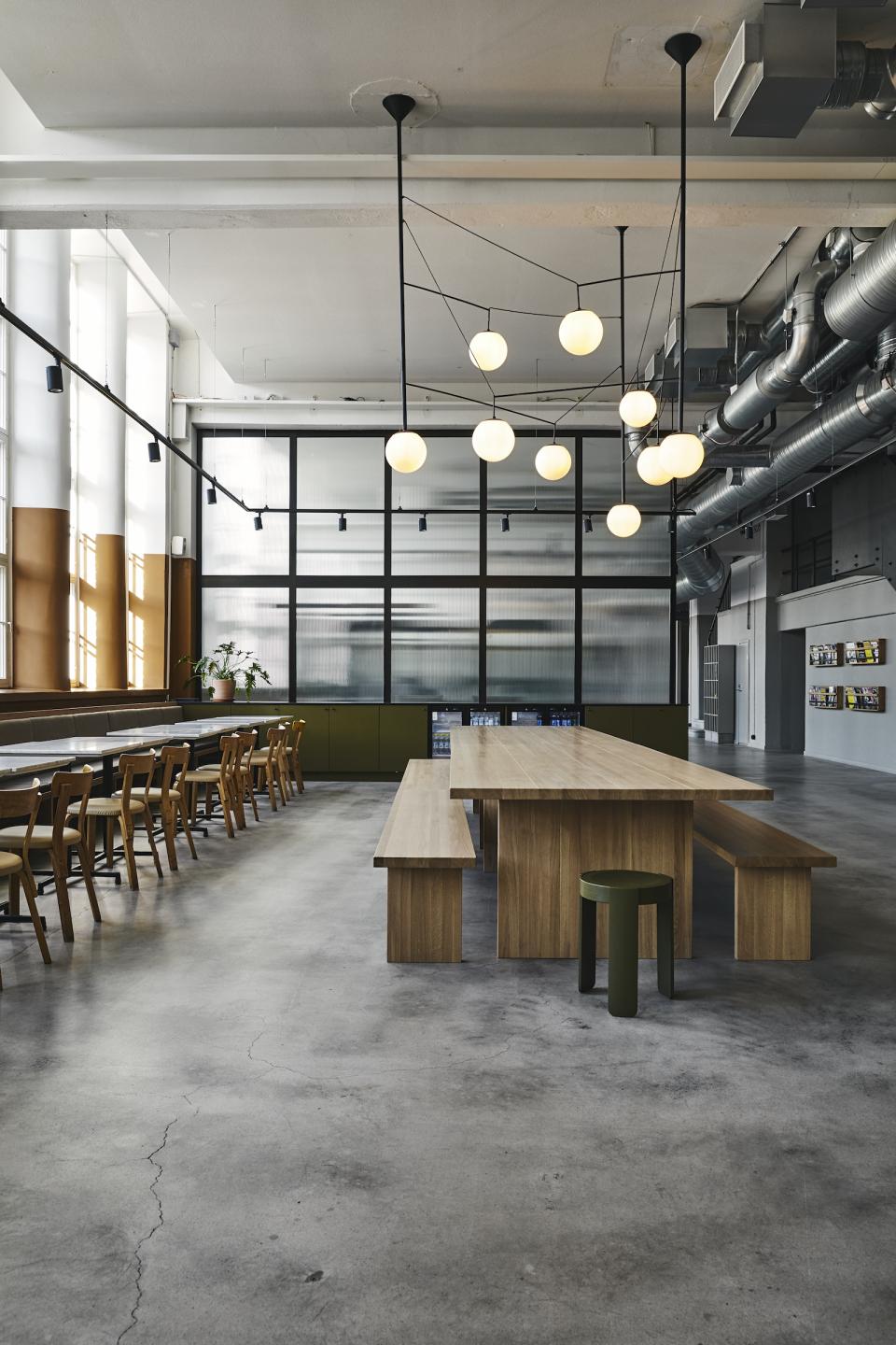 Spacious refurbished interior of an old bread factory featuring minimalist furniture and modern lighting by Studio Joanna Laajisto.