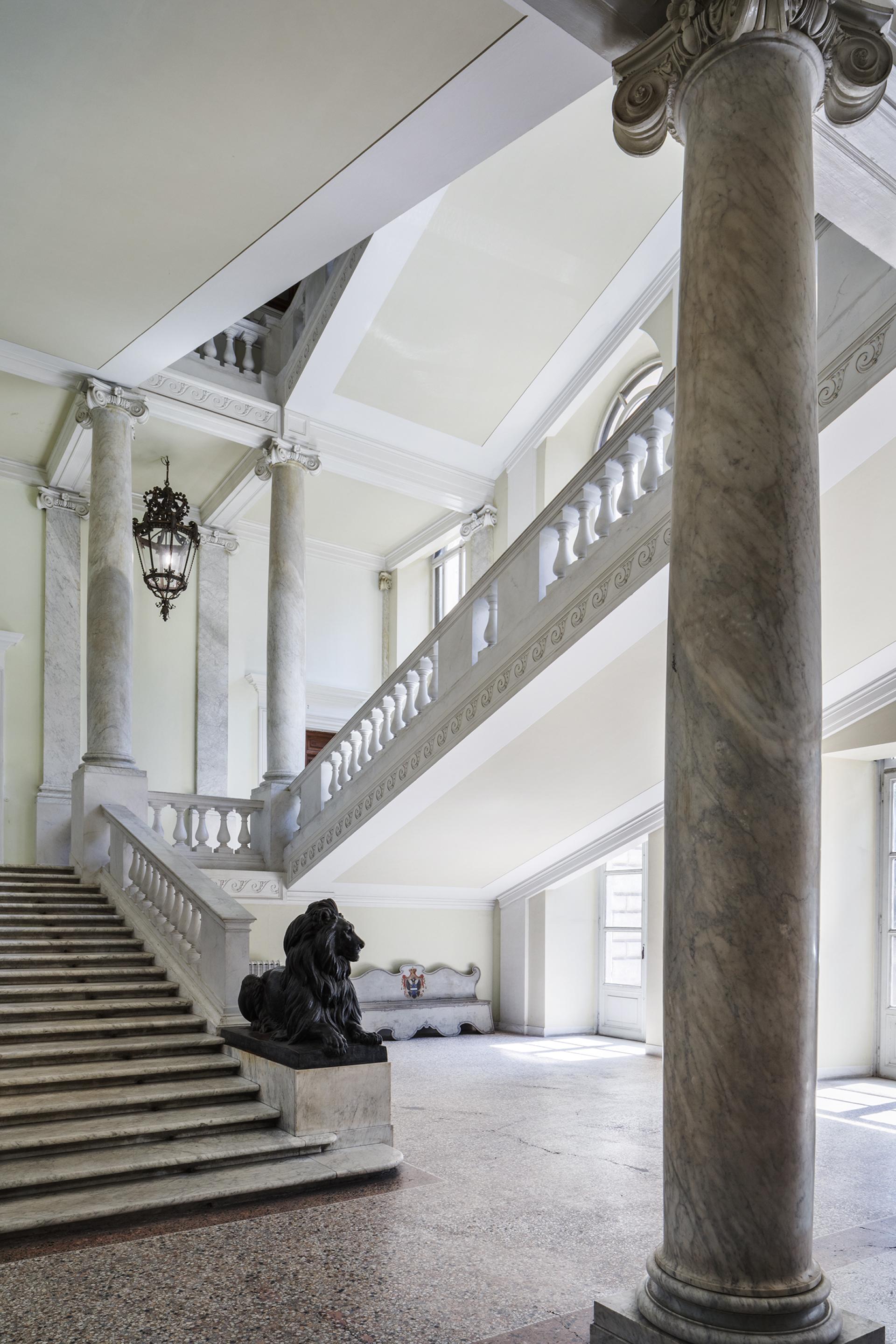 Elegant interior of Palazzo Brancaccio featuring grand marble stairs, intricate columns, and a lion statue, highlighting Contemporary Cluster's new space.