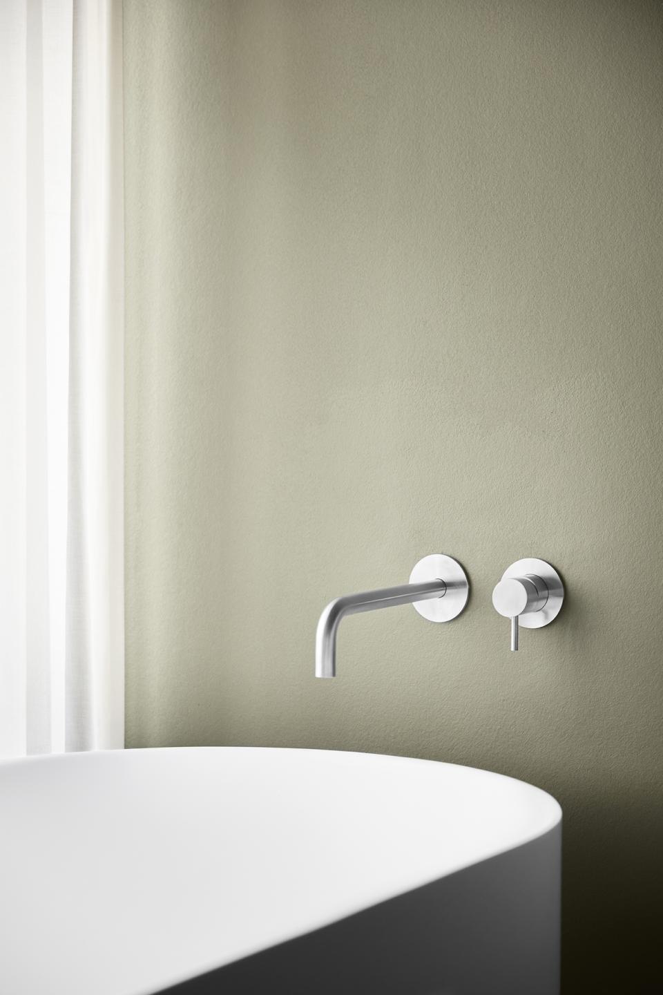 Sleek wall-mounted faucet and minimalist bathtub against a soft green wall, highlighting d line's Qtoo collection design.