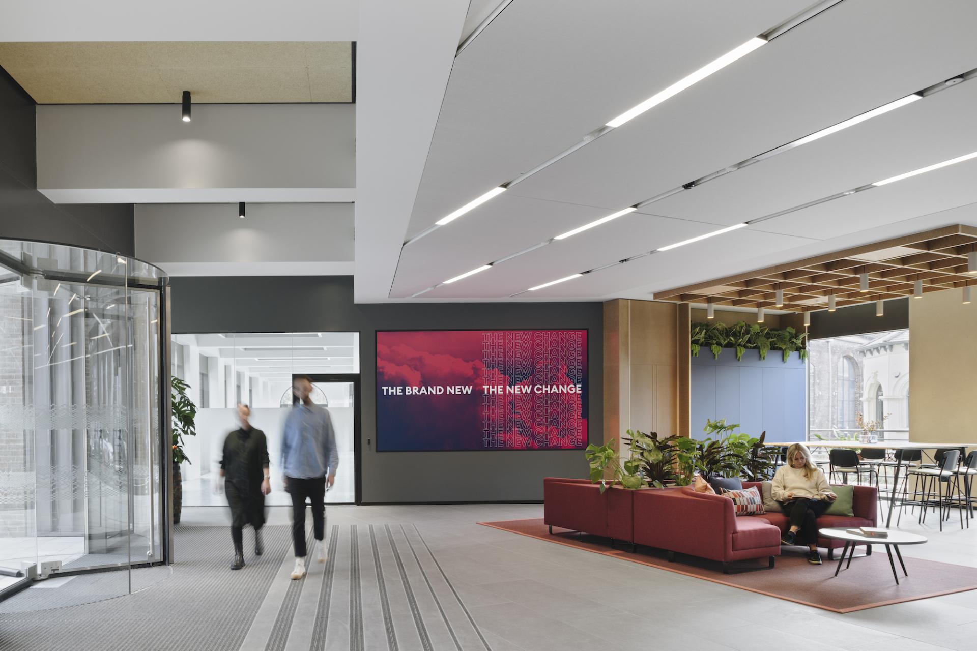 Modern industrial lobby design at Globe Point, featuring a vibrant digital display and inviting seating area by Ekho Studio.