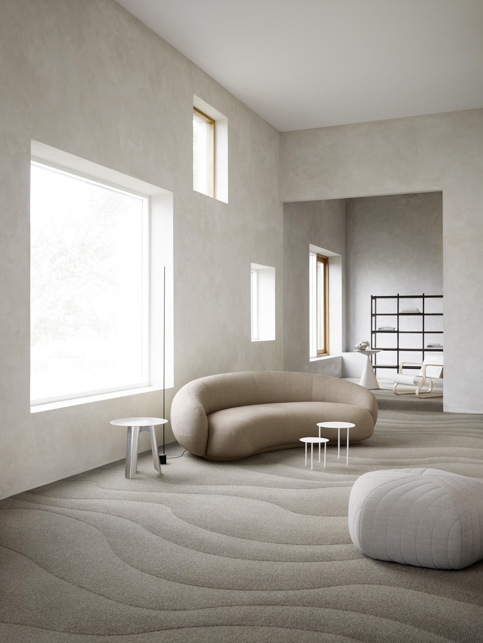 Minimalist interior featuring a curved beige sofa, modern furniture, and textured flooring in a sustainable design studio.