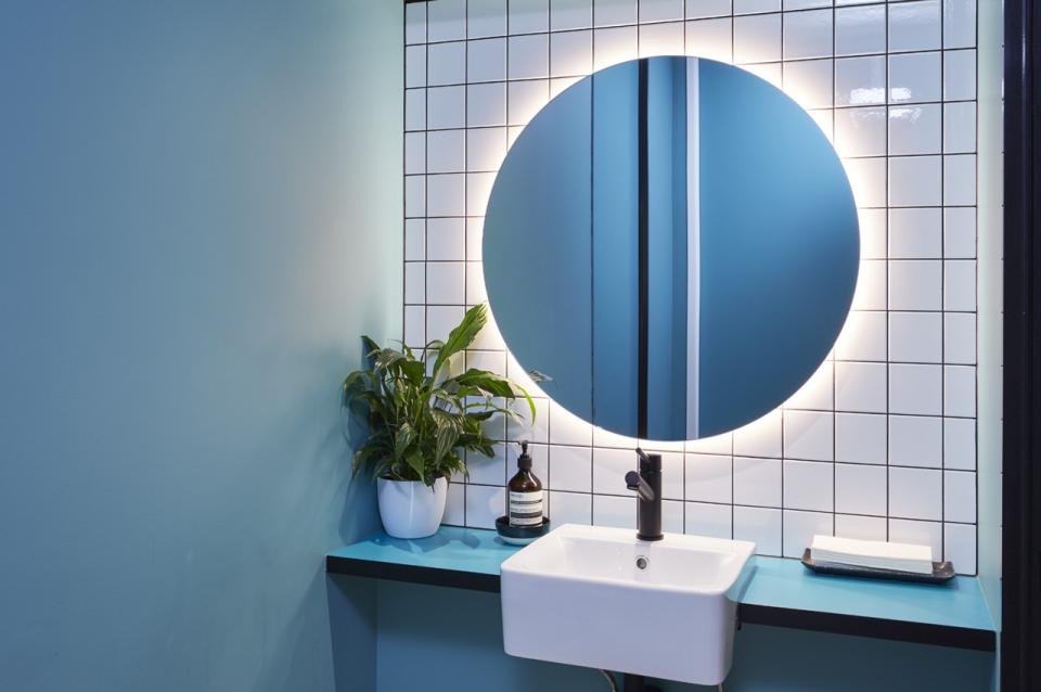 Modern bathroom design featuring a circular mirror, vibrant colors, and greenery, enhancing the workspace ambiance.