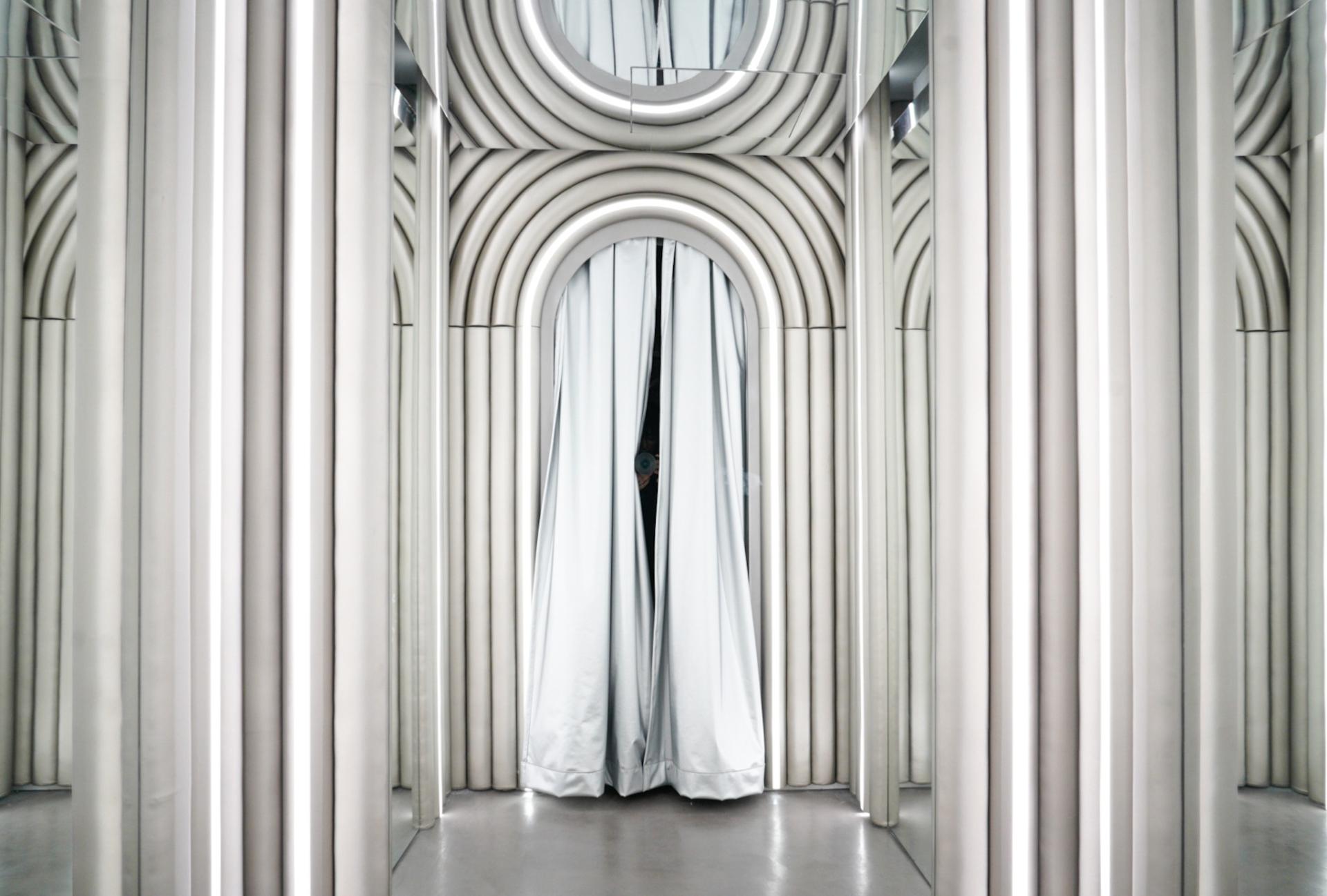 A contemporary interior featuring curved, mirrored columns and draped curtains, showcasing Masquespacio's design for MO espresso bar.