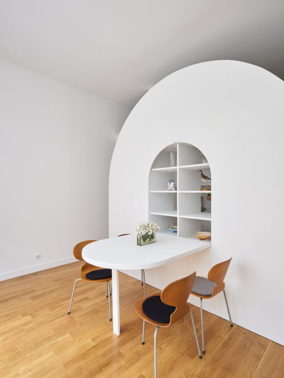 Modern dining area featuring a rounded white wall shelf and minimalist furniture in a Parisian home.