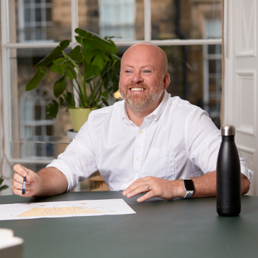 Michael McGurk, project director at MLA, discussing challenges in Scottish residential renovations with a project plan on the table.