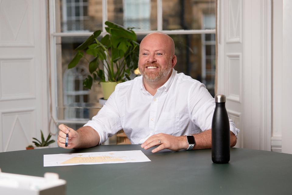 Michael McGurk, project director at MLA, discussing challenges in Scottish residential renovations with a project plan on the table.