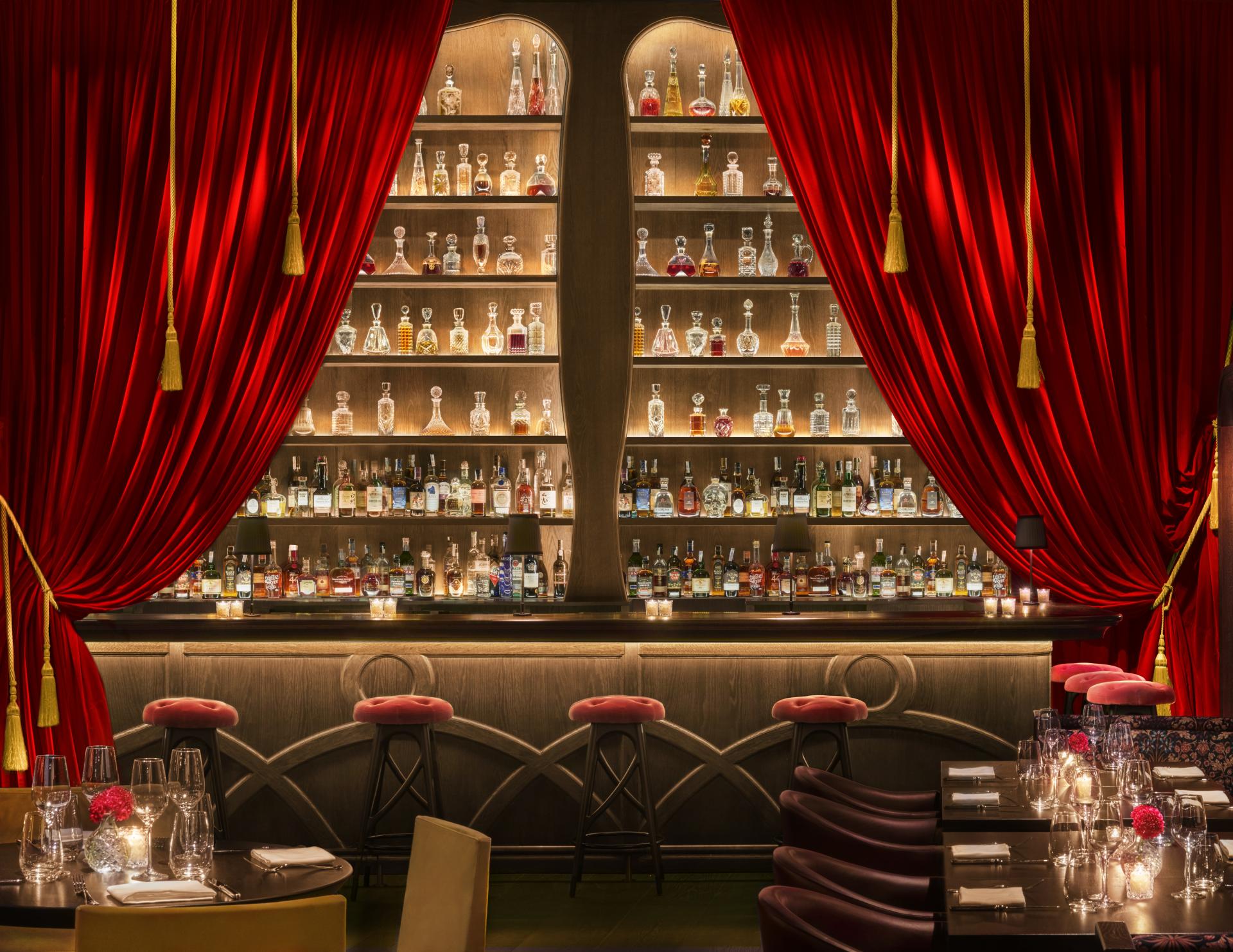 Elegant bar area at Barcelona EDITION featuring a colorful array of spirits, plush seating, and luxurious red curtains.