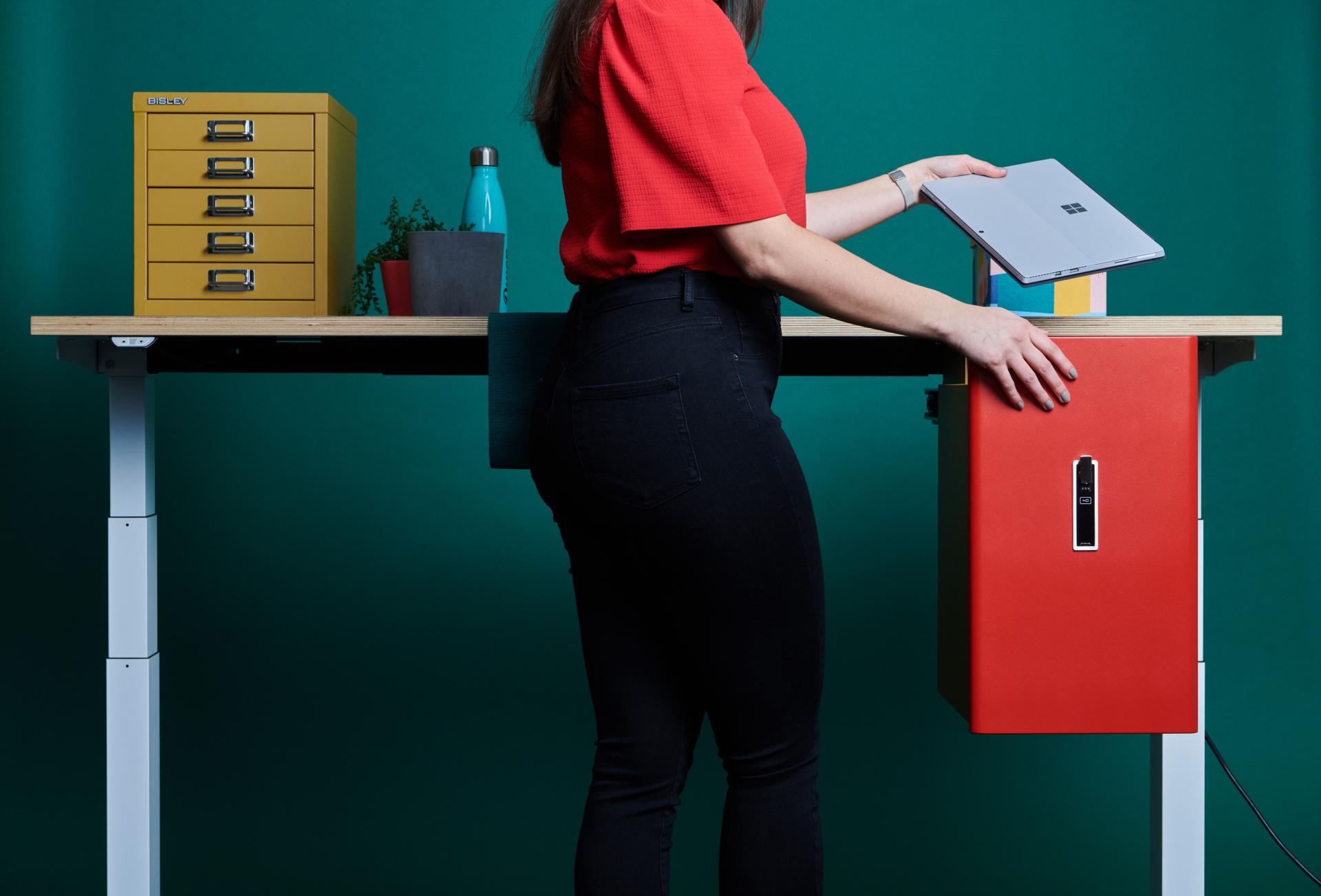 A woman interacts with the colorful Bisley Buddy storage unit at a modern standing desk.