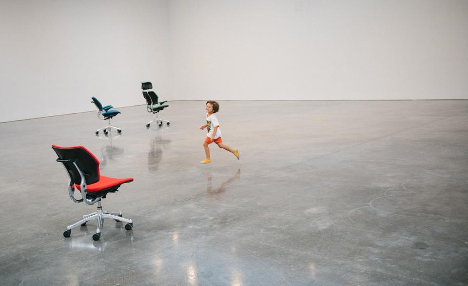 A child runs playfully among Humanscale's Freedom chairs in a spacious, minimalist exhibition space.