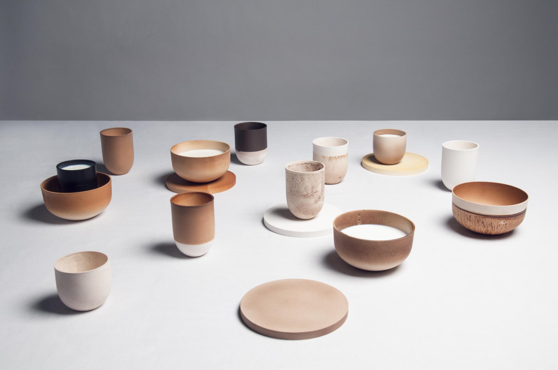 Handcrafted biomaterial cups and bowls in various natural colors arranged artistically on a light grey background.