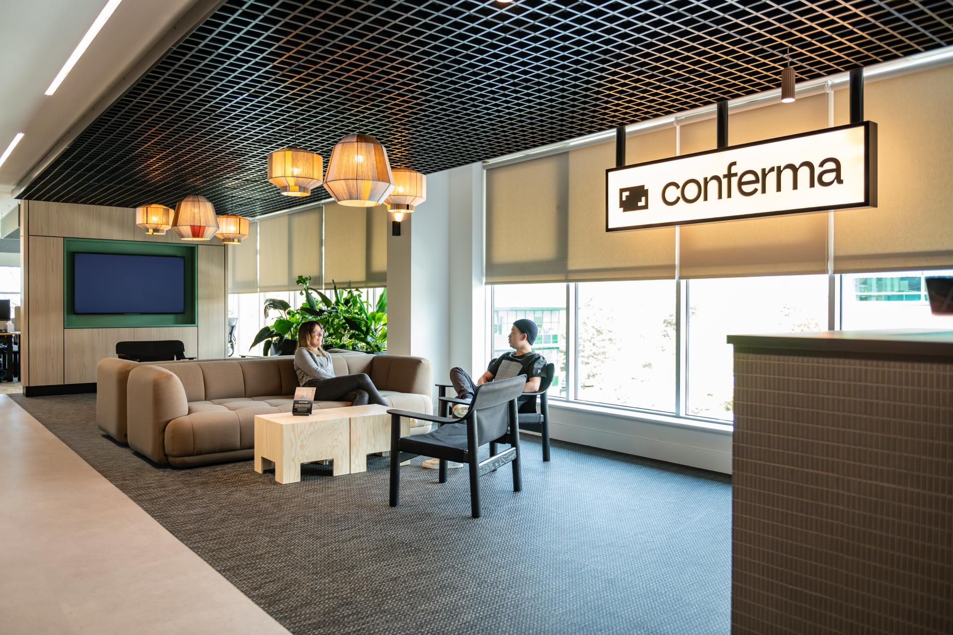 Modern office space at Conferma featuring a cozy seating area and large windows, emphasizing a collaborative work environment.