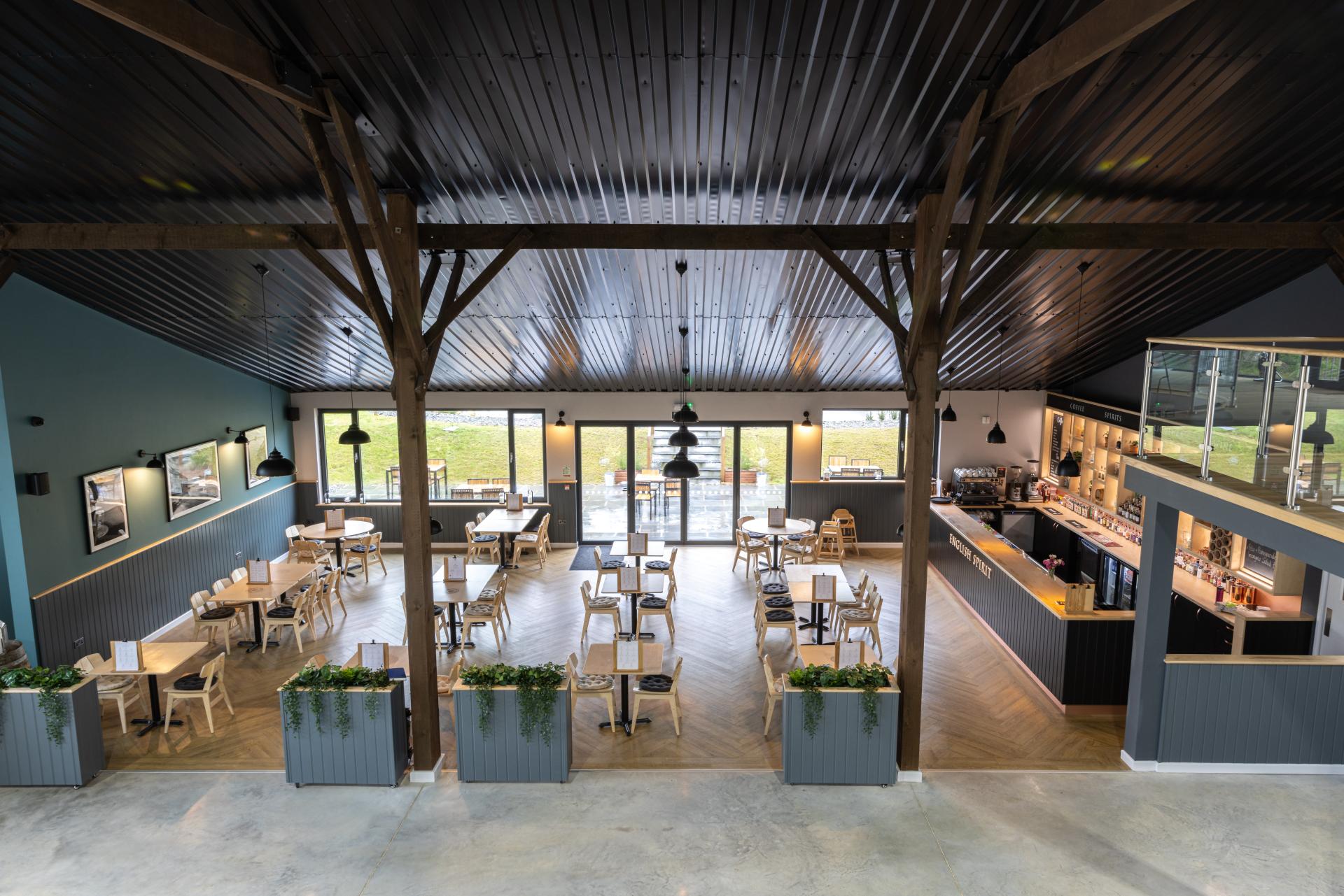 Modern interior of The English Spirit Distillery featuring wooden tables, bar area, and large windows for natural light.