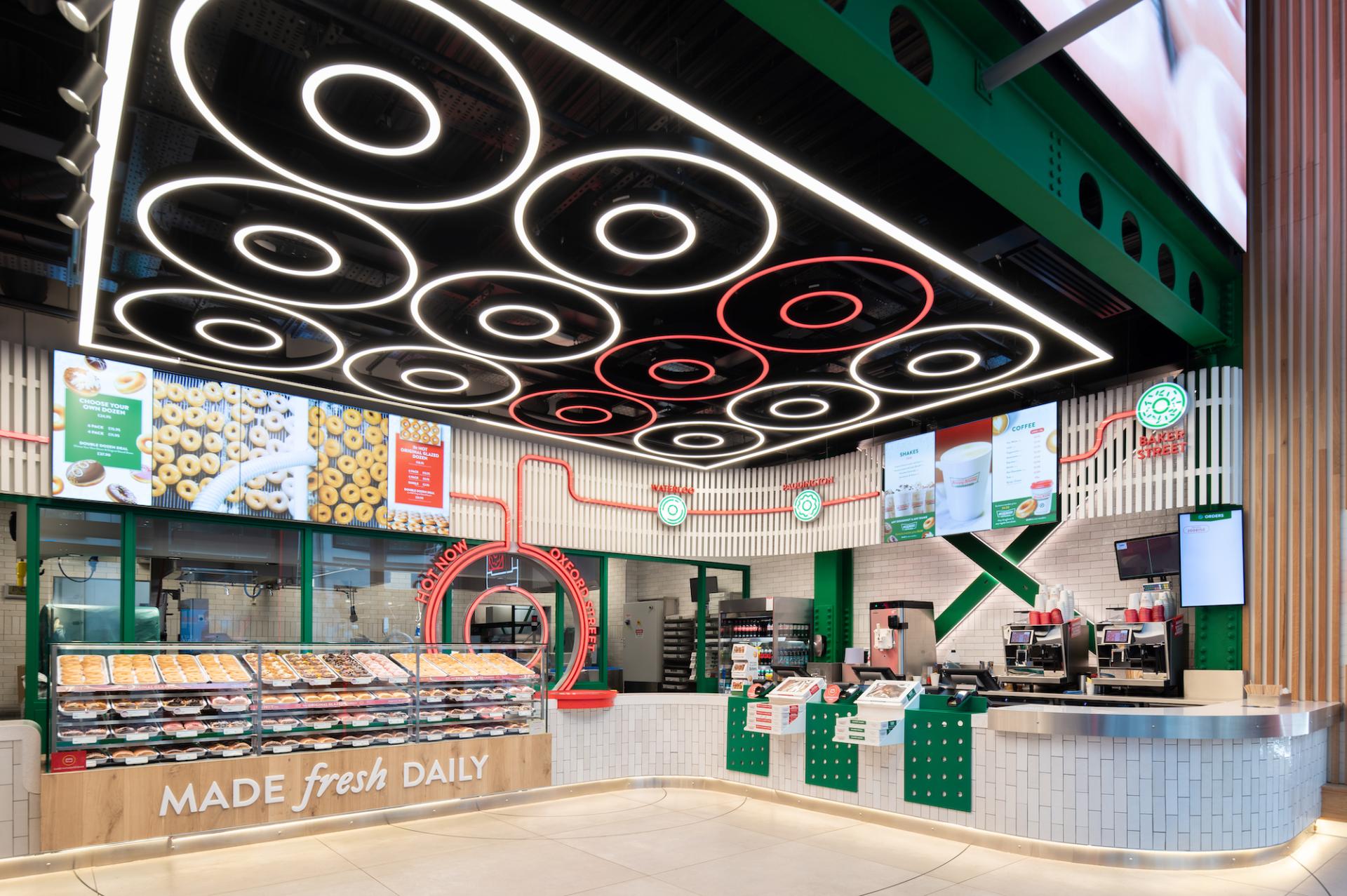 Brightly lit interior of Krispy Kreme's London flagship store, featuring an illuminated ceiling and display of fresh donuts.