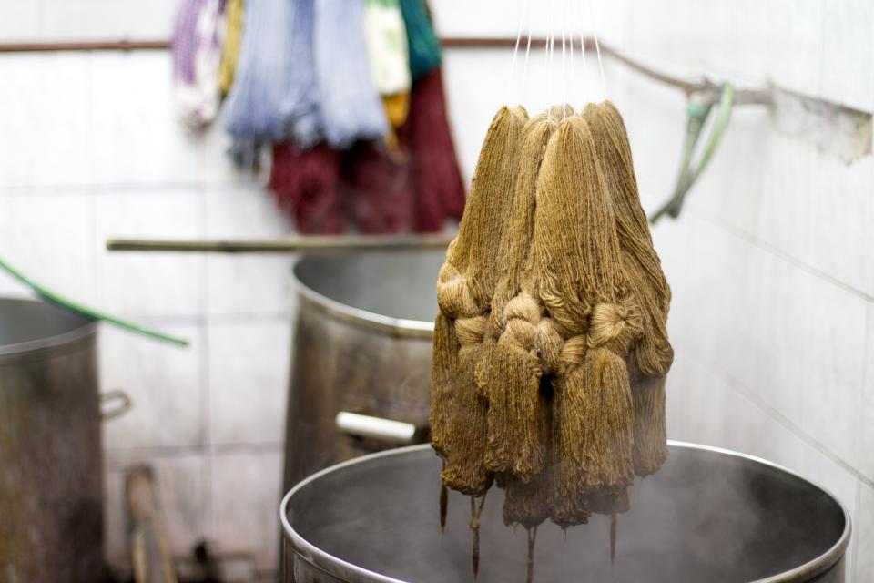 Skeins of natural wool being dyed in large metal pots, part of the crafting process for Carolina Palombo’s Tutura chair.
