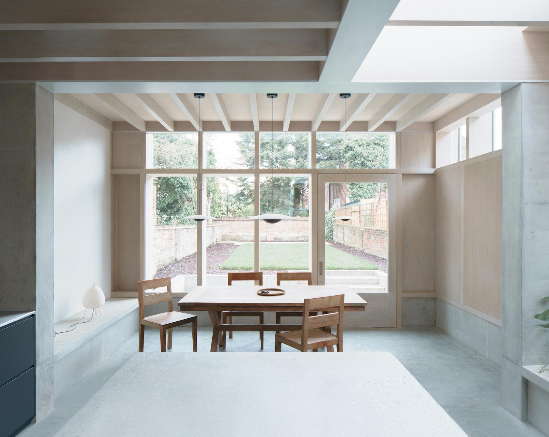Bright, modern dining area in Concrete Plinth House featuring wooden furniture, large windows, and views of the garden.