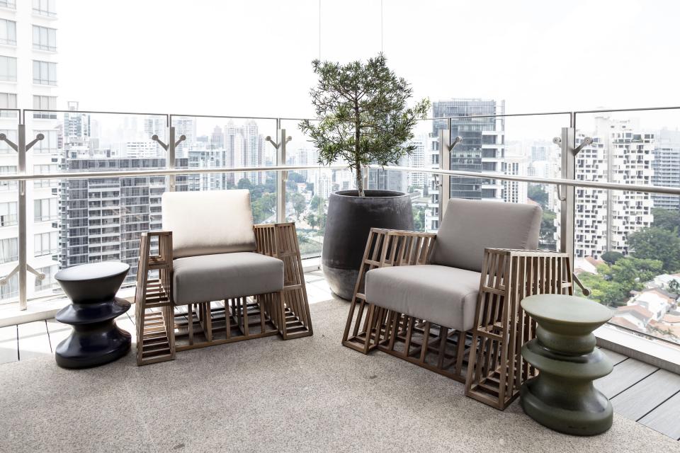 Stylish balcony seating with modern chairs and decorative planters overlooking Singapore's skyline, showcasing interior design by Elliot James.