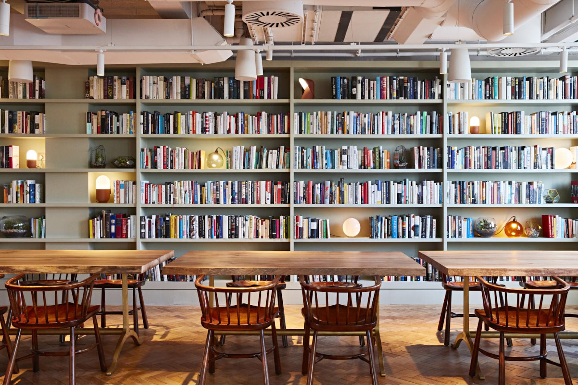Cozy reading area with bookshelves, wooden tables, and chairs in The Conduit Members Club's Scandinavian-inspired interior.