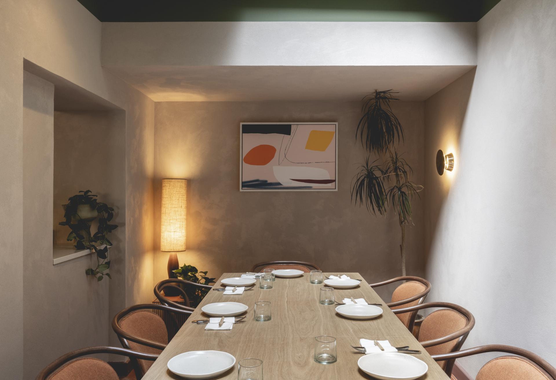 Cozy dining area at Honey & Co Bloomsbury, featuring a wooden table, stylish chairs, artwork, and ambient lighting.