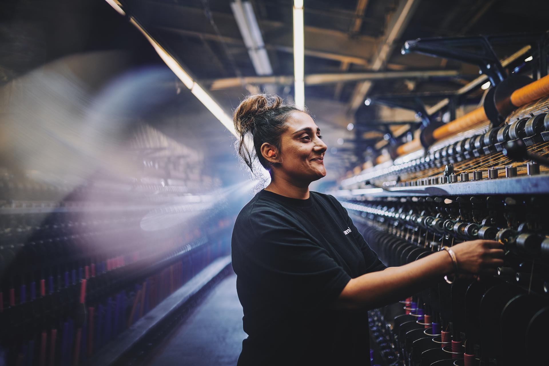 Worker smiling while operating textile machinery in a sustainable British manufacturing facility, highlighting Camira's commitment to eco-friendly practices.