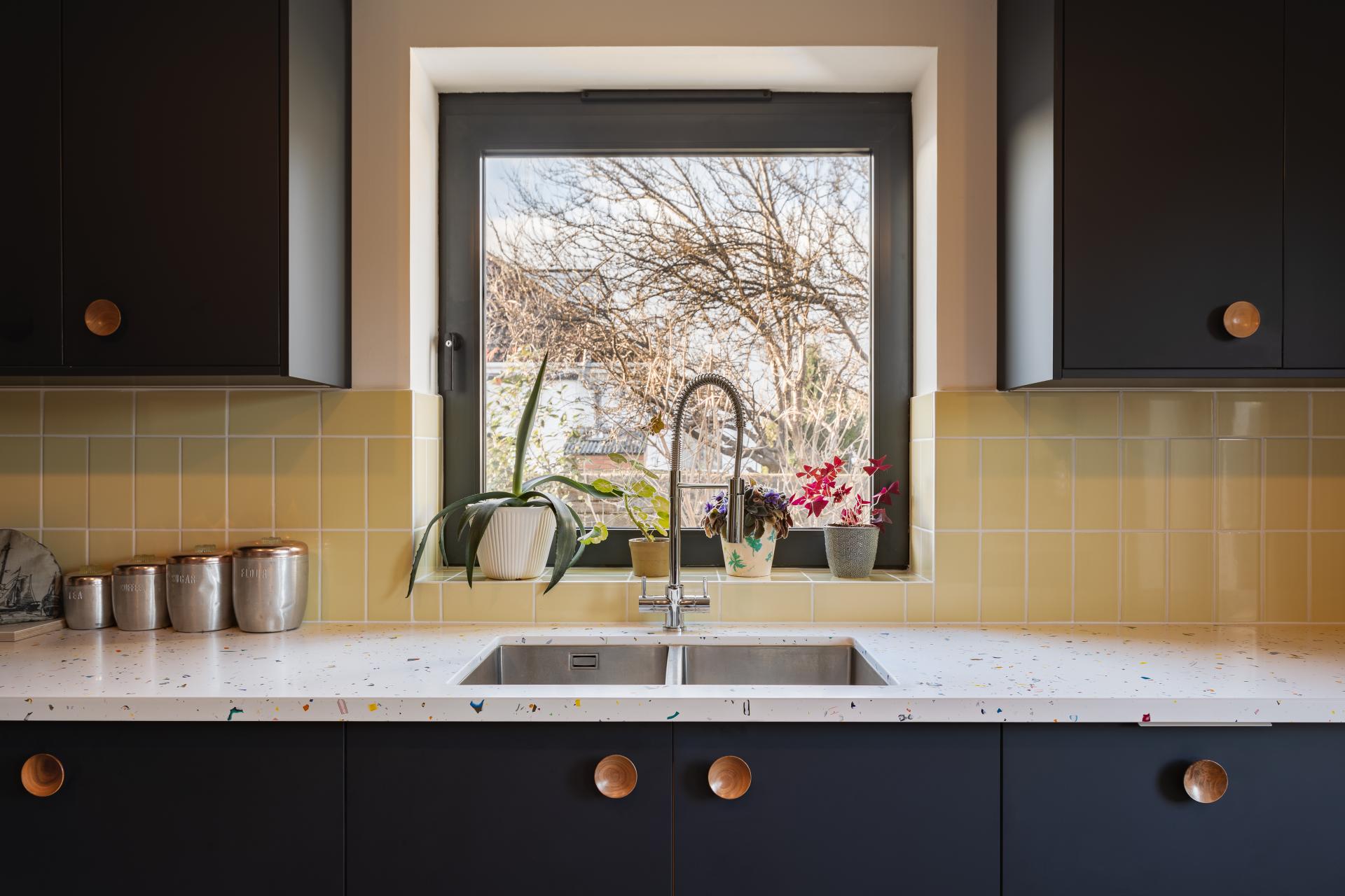Modern kitchen featuring a stylish sink, colorful countertop, and potted plants near a bright window.