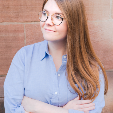 Stephanie Taylor of M1NT Studio is posing confidently with arms crossed against a textured stone backdrop.