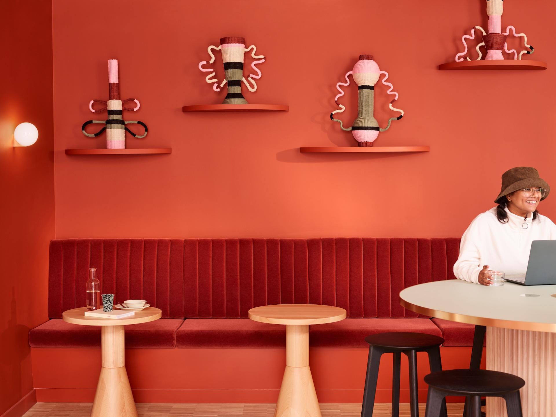 Stylish interior of Liberty House workspace featuring vibrant red decor, modern seating, and a woman working on a laptop.
