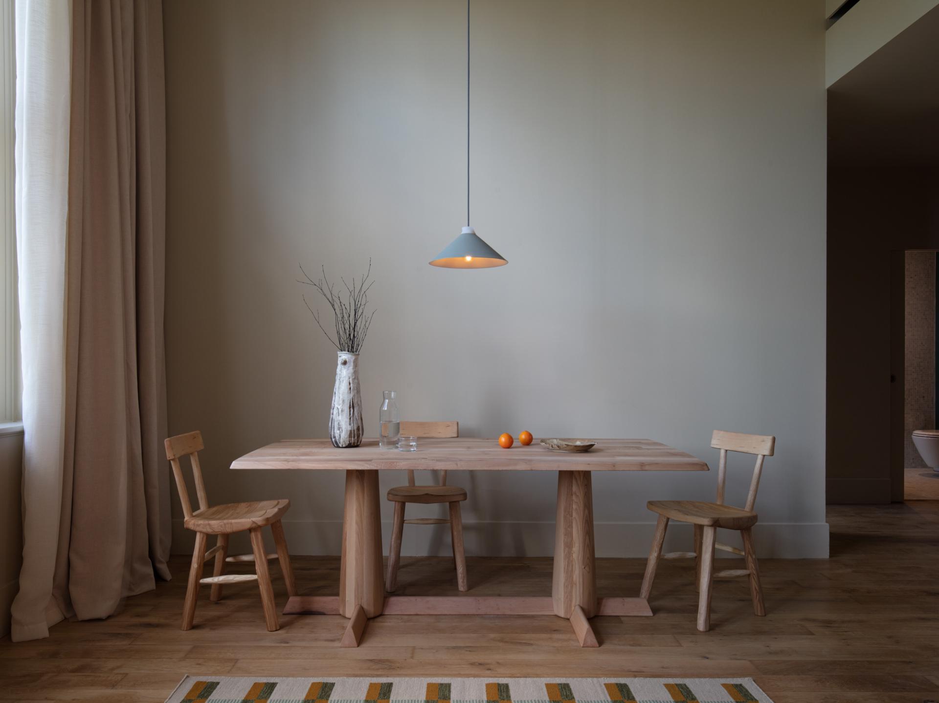 Minimalist wooden dining table with three chairs, a vase, and decorative elements in a serene interior setting.
