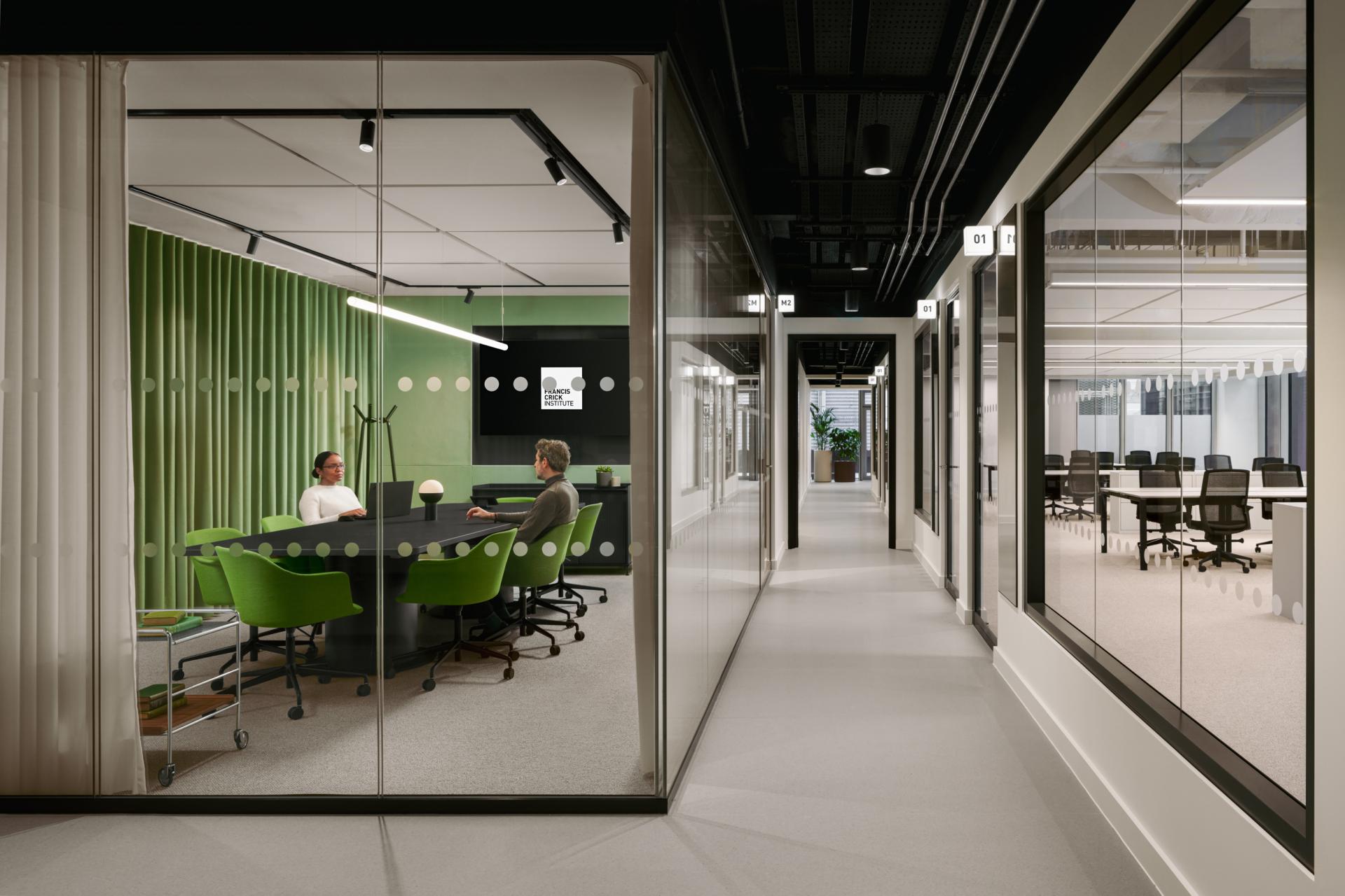 Modern office interior showcasing a collaborative meeting space, featuring green accents and glass walls, emphasizing design for nature and neurodiversity.