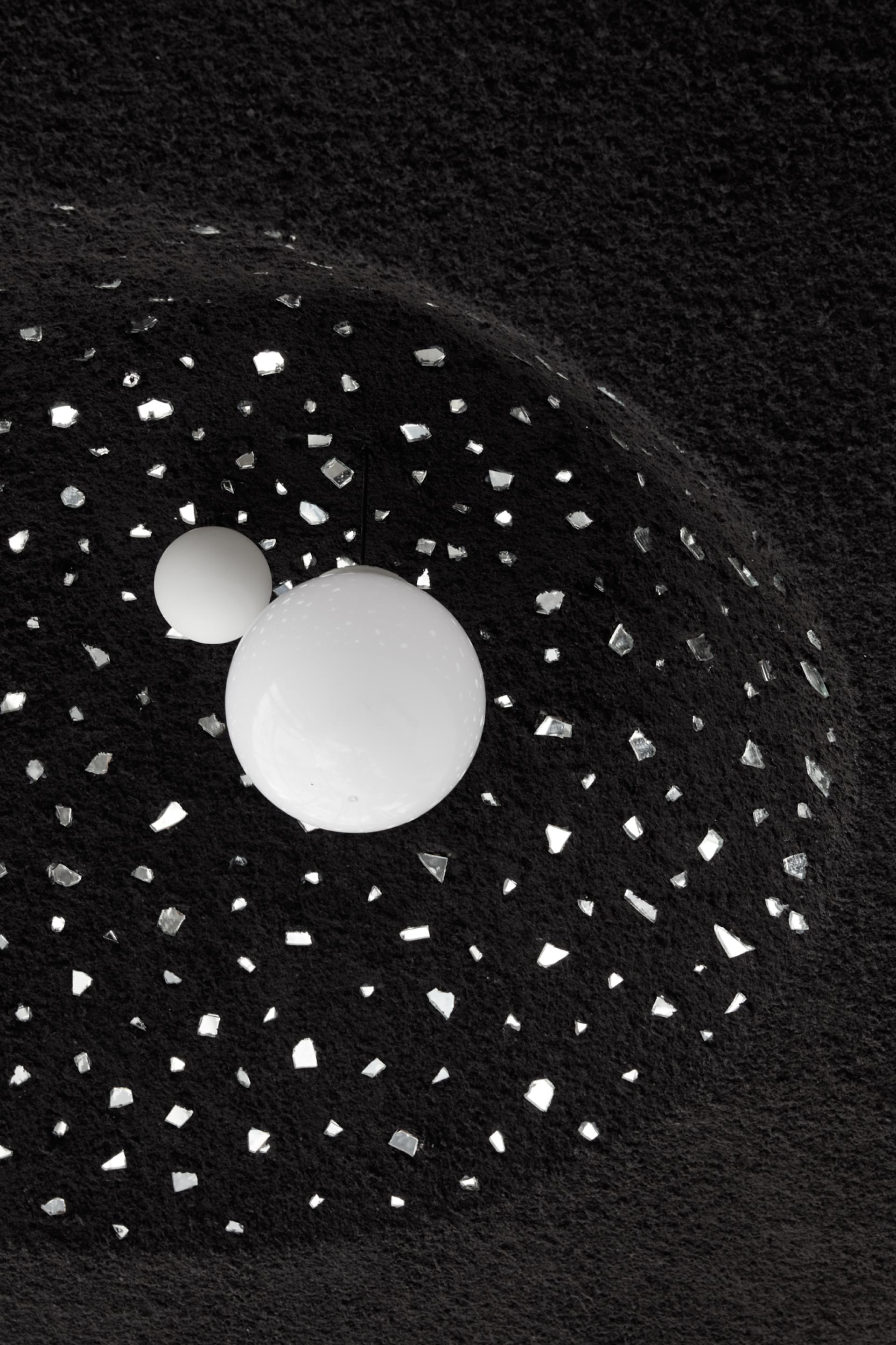 Textured black wall featuring white spherical lamps among scattered silver mirrors, highlighting the minimalist design of Drop Coffee in Abu Dhabi.