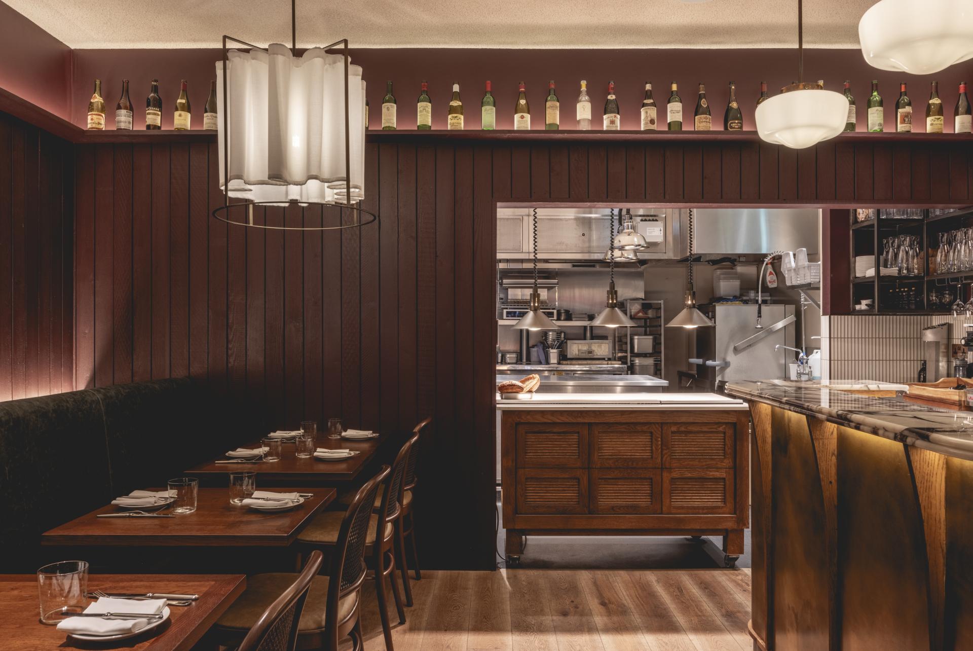 Elegant Fitzrovia restaurant interior featuring wooden accents, Parisian-inspired decor, and a glimpse of the open kitchen.