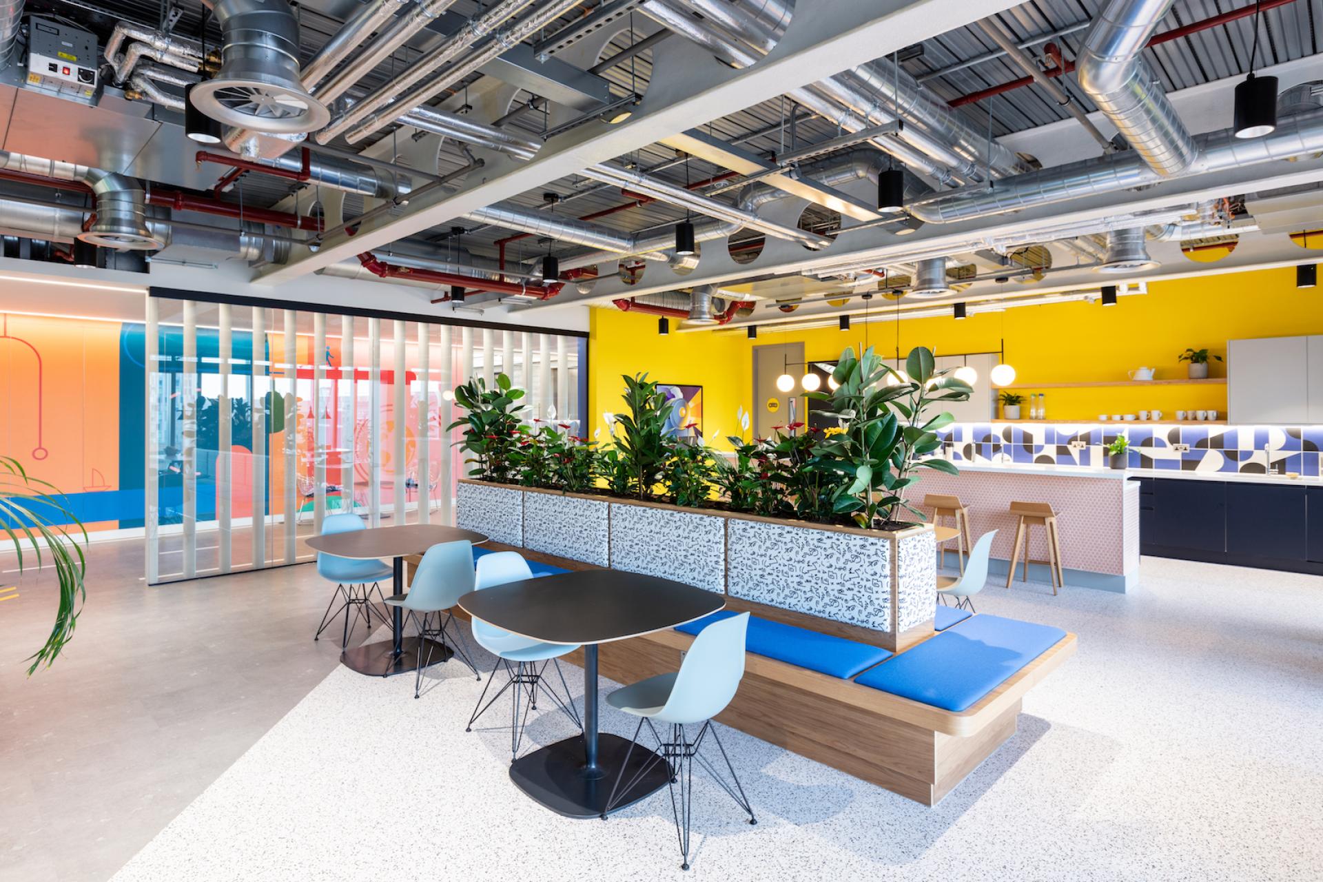 Vibrant modern office space featuring stylish seating, indoor plants, and colorful decor, designed by Modus for Travelfusion.