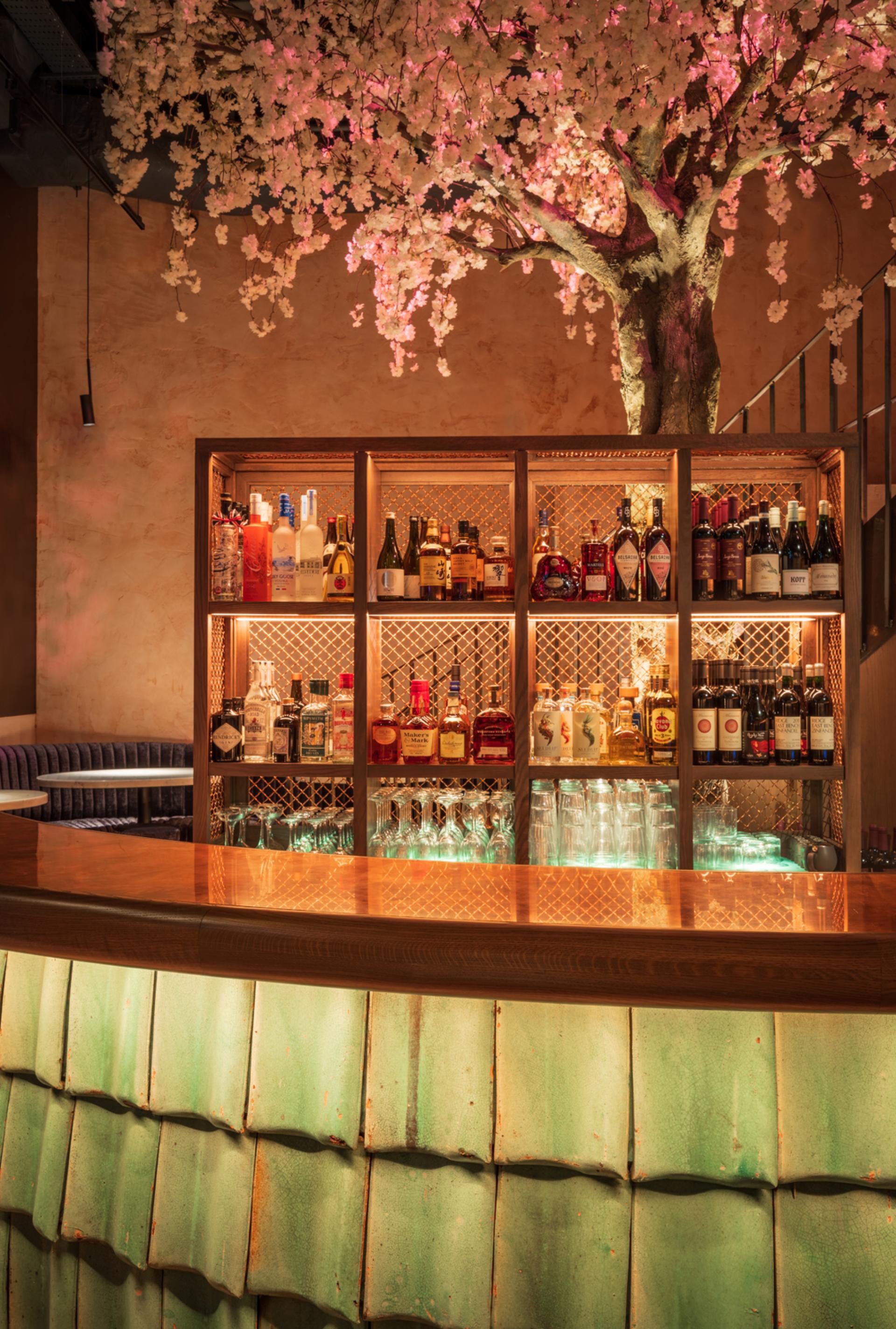 Elegant bar design at Andrew Wong's restaurant features a vibrant display of spirits and decorative cherry blossom tree.
