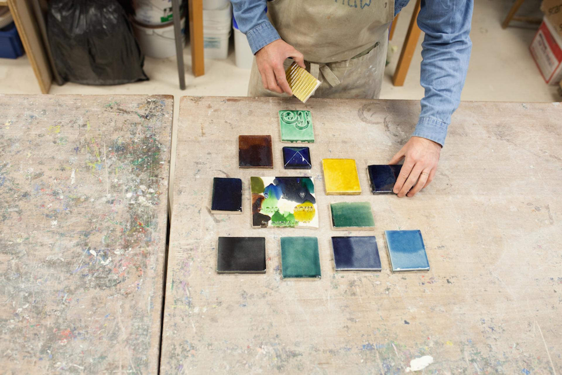 Ceramic artist Matthew Raw arranging colorful clay tiles on a workbench in his studio.
