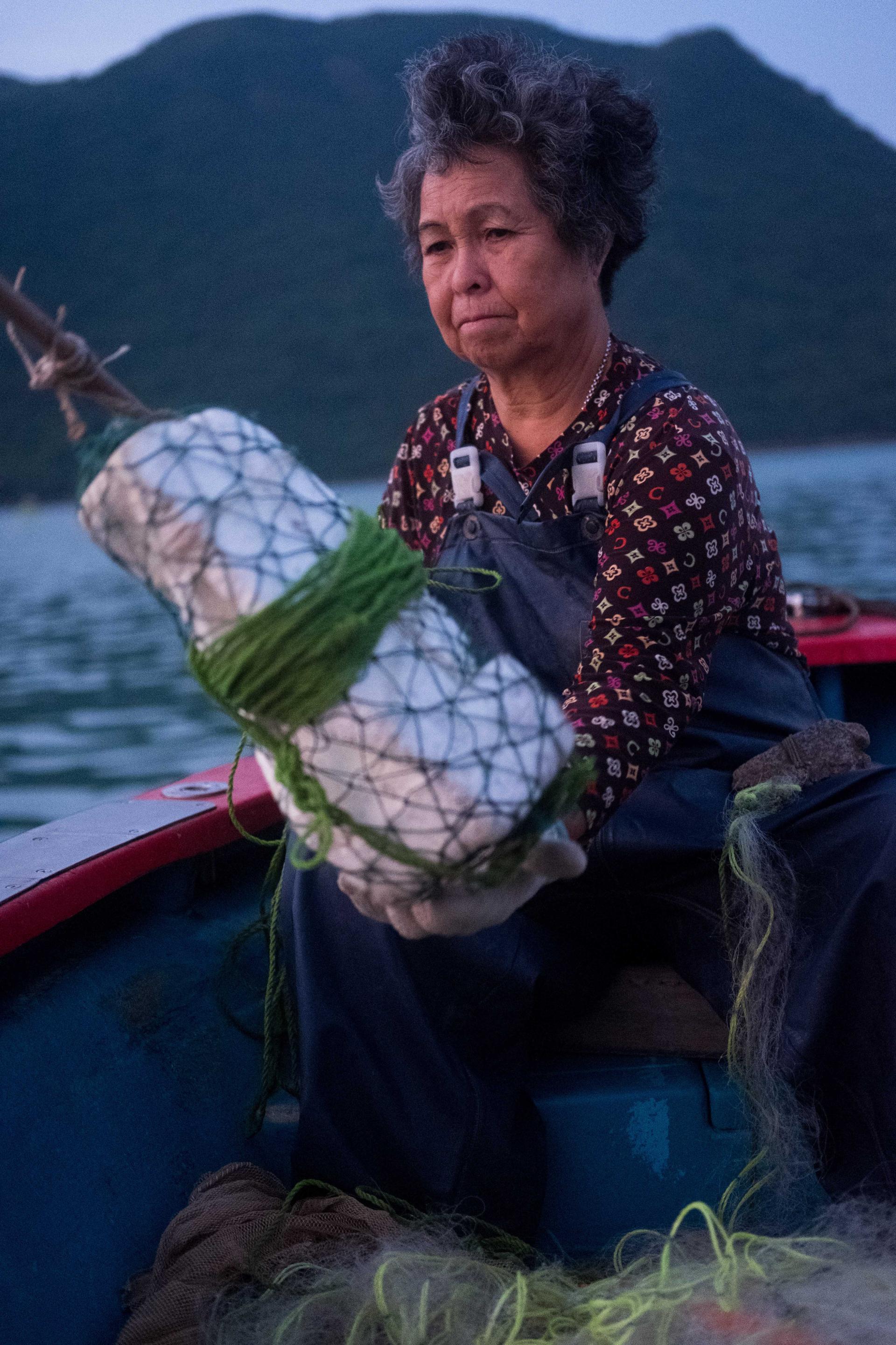 A woman in a boat holds a wrapped bundle, showcasing traditional craft techniques using local waste materials.