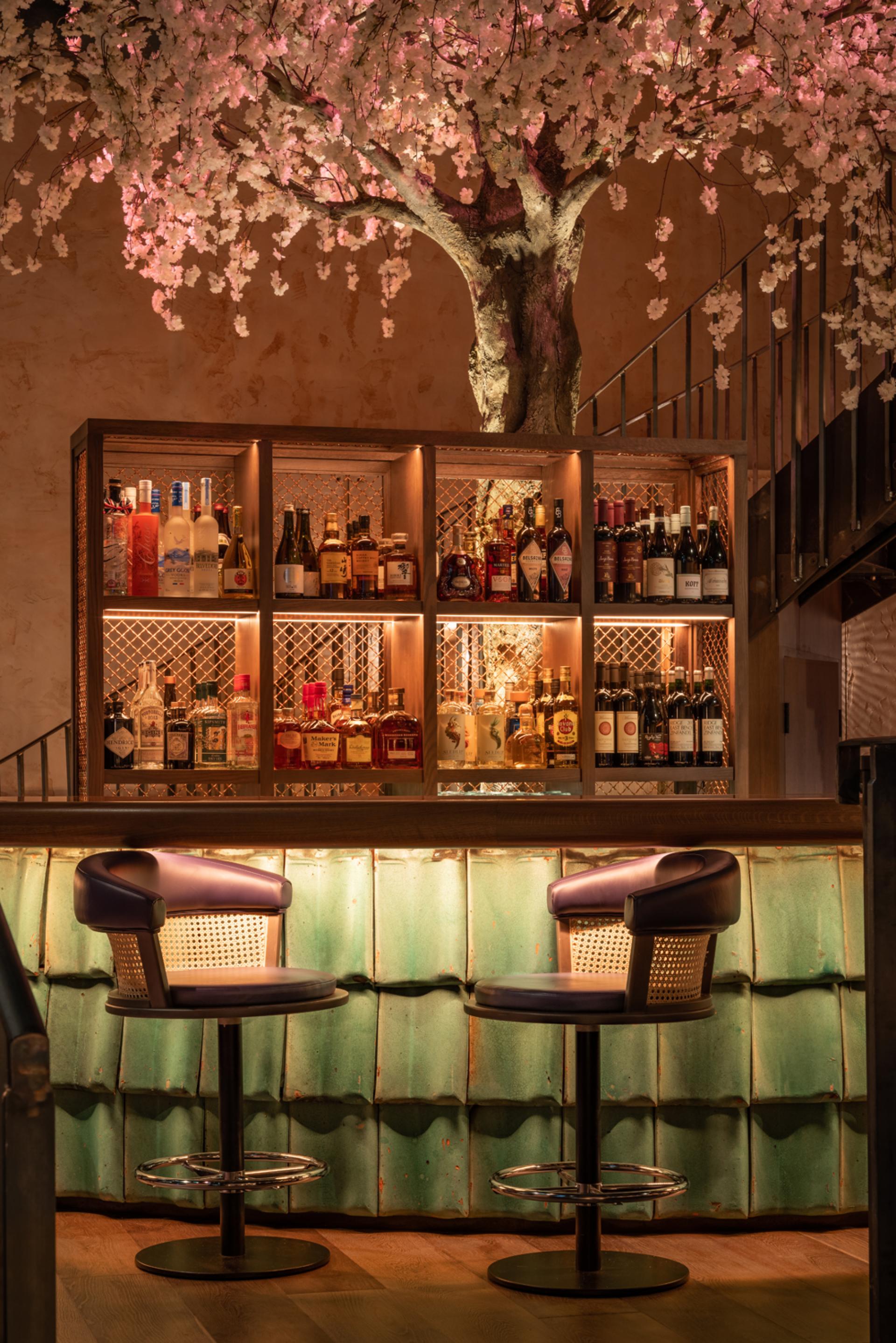 Stylish bar area featuring a decorative cherry blossom tree, displaying a curated selection of fine spirits at Andrew Wong's restaurant.