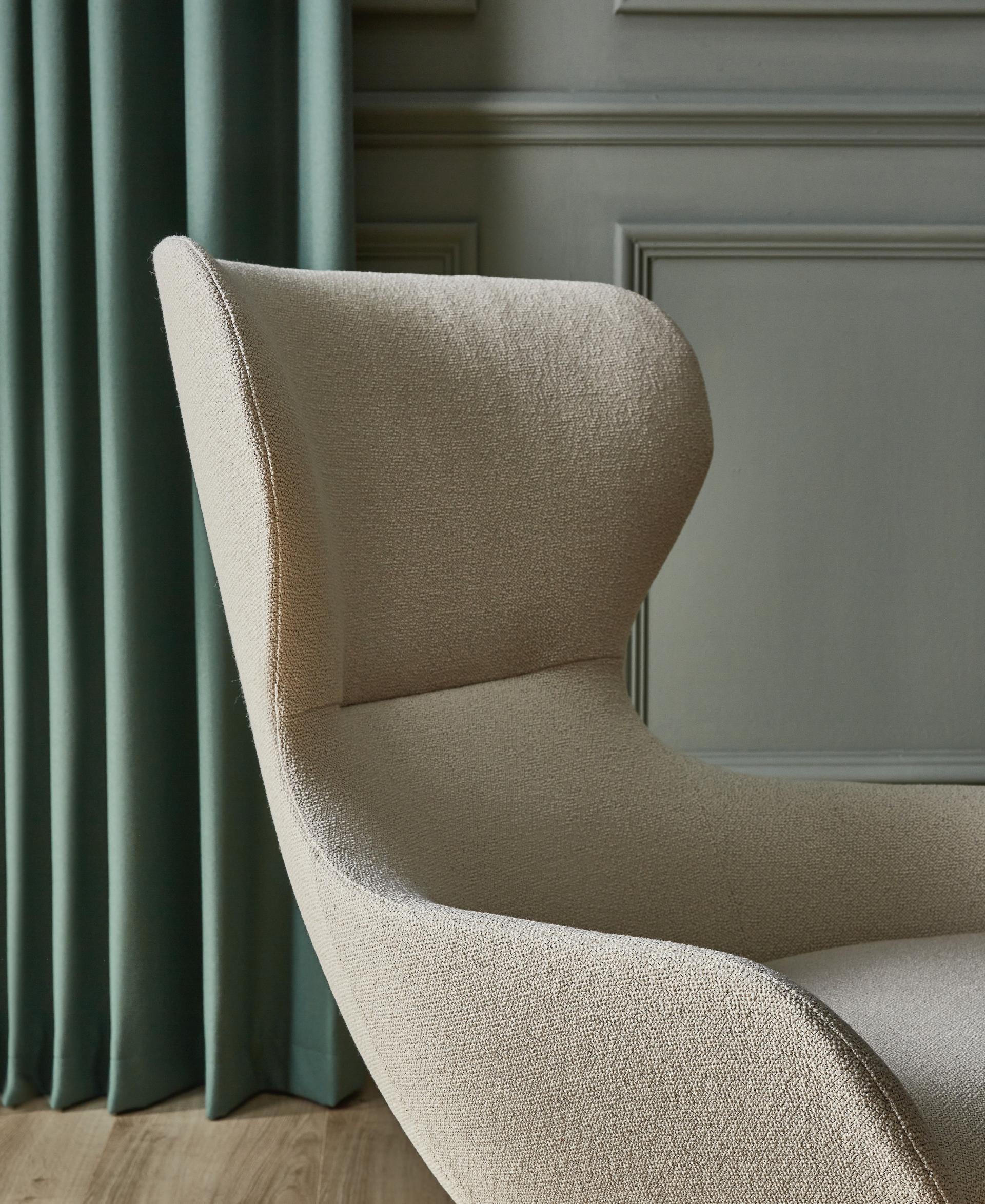 Elegant beige bouclé chair in a stylish interior setting with green curtains, showcasing Camira's new spring colors.
