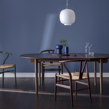 Wishbone chairs in nature-inspired colors arranged around a classic dining table against a serene blue wall backdrop.