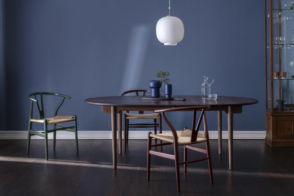 Wishbone chairs in nature-inspired colors arranged around a classic dining table against a serene blue wall backdrop.