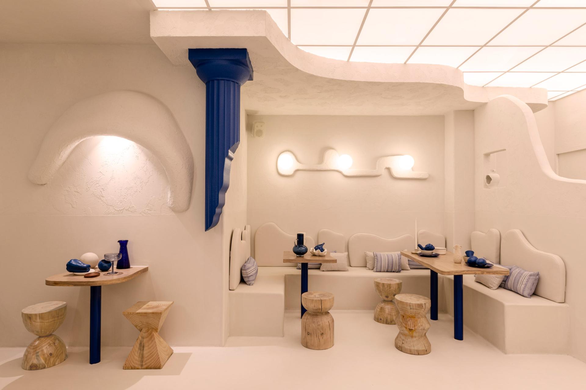 Modern Greek restaurant interior showcasing white walls, blue accents, unique seating, and artistic decor elements.