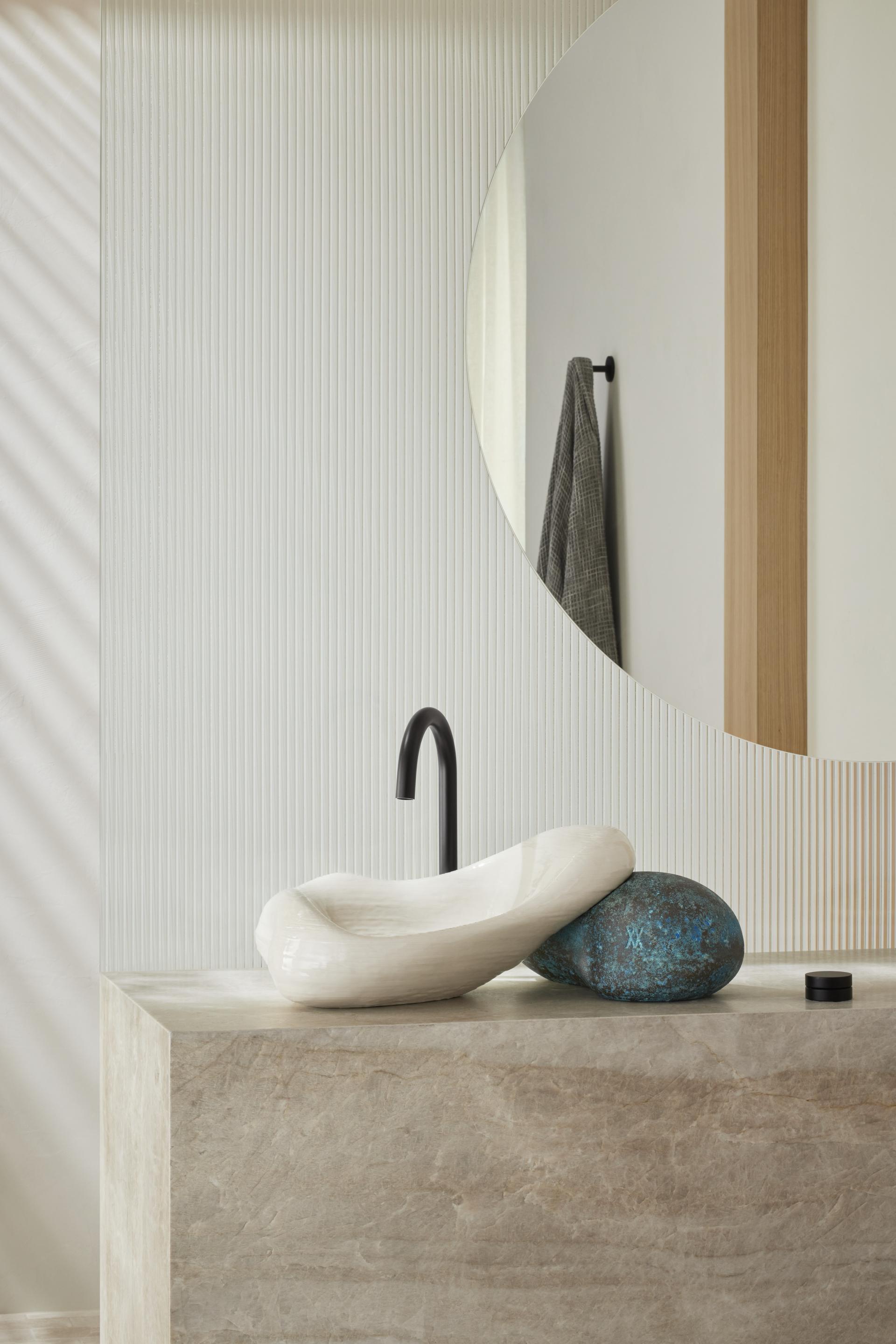 Sleek, white 3D-printed sink by Kohler and Daniel Arsham, featuring a unique design atop textured stone surface.