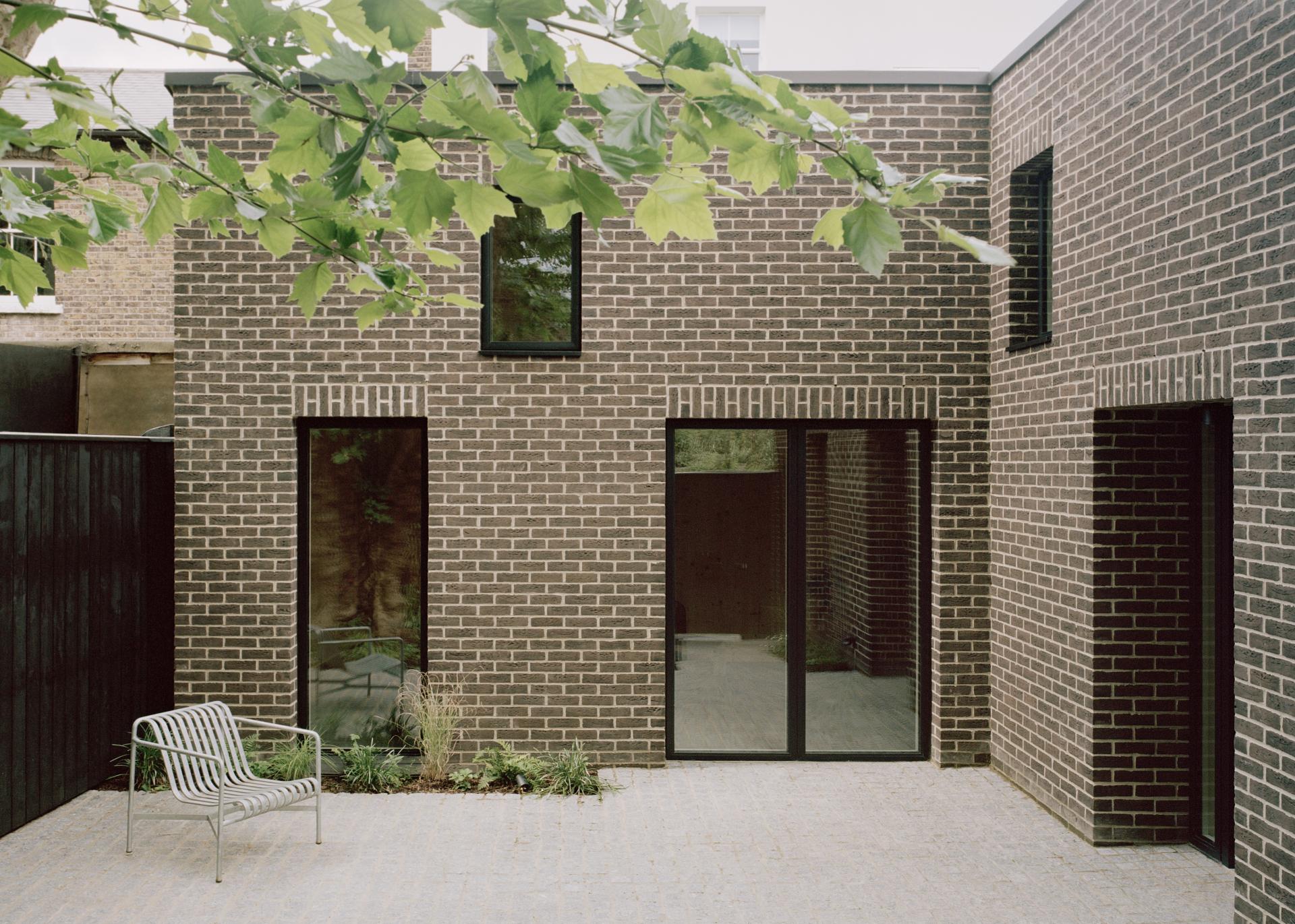 Sustainable Tree Courtyard House features a brick façade, modern windows, and a minimalist outdoor seating area.