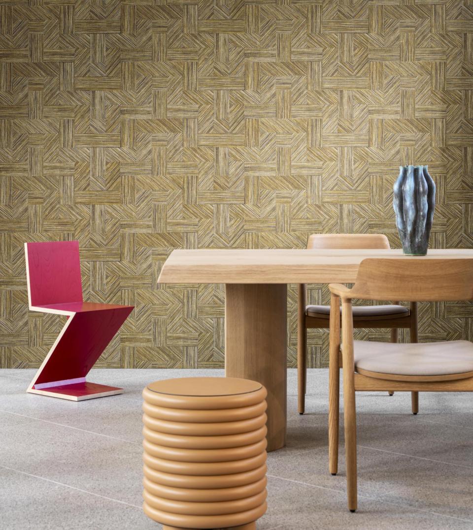 Modern dining area featuring a unique pink chair, wooden table, cylindrical stool, and textured golden wall inspired by Tangram designs.